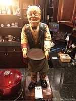 Full view of the hand-painted butler figurine holding a serving tray, standing on a wooden base with a label.