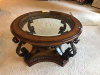 Full view of the round glass top coffee table showing wooden frame and metal scroll base resting on carpet.