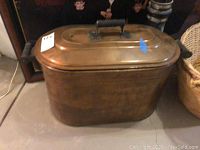 Copper boiler with lid and black side handles shown from side angle.