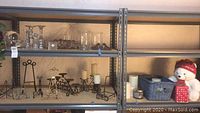 View of three shelves displaying metal and glass candle holders, wire decorative stands, blue basket, and a festive white bear.