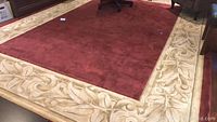 Full view of the rug laid out on a hardwood floor showing the burgundy field and cream decorative border