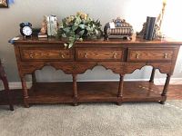 Front view of oak console table showing three drawers, scalloped apron, turned legs, lower shelf and decorative items on top