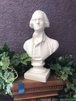 Alva bust of Thomas Jefferson on wood surface surrounded by greenery.