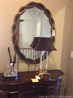 Photo showing wall mirror, lamp, and eagle statue arranged on and above wooden cabinet