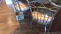 Two metal swivel bar stools pictured from side showing full height and narrow width, with plaid cushions and bar frame foot rests