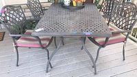 Full view of metal patio table with four metal chairs having cushioned seats, showing outdoor placement and overall condition.