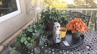 Outdoor table displaying various outdoor decor items including artificial greenery, pots, a ceramic dog figurine, and a white oscillating fan