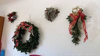 Seven Christmas wreaths and a hanging snowman welcome sign displayed on a white wall.