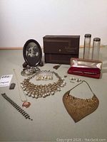 Overview photo of the full lot including jewelry, keepsake items, pen with case, photo frame, glass cylinders, and box
