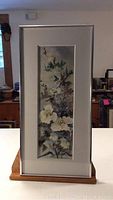 Full view of the framed vertical watercolor painting of flowering plant.