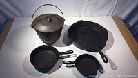 Top view of four cast iron items: a caldron with lid and handle, large Wagner USA skillet, two smaller Taiwan skillets.