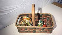 Full view of the woven Easter basket containing several decorative eggs including vintage paper and hand-painted wooden eggs.