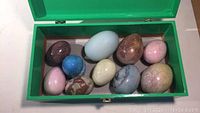 View of all 10 polished stone eggs arranged inside a green box, showing various colors and sizes