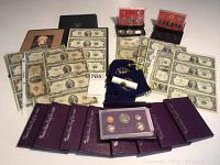 All coins and currency spread on tabletop showing proof sets, nickel rolls, uncut sheets, and various bills