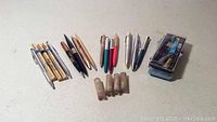 Collection of over 20 pens and mechanical pencils arranged in groups by type and color, including multiple gold and metallic pens, and 5 tubes of replacement lead. Also includes a box with Cross pens and cartridges.