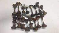 Top view of multiple rows of antique doorknobs laid out in rows showing glass, brass, wooden and porcelain pieces attached to mounting spindles on white surface.