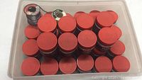 Plastic container holding 32 containers with red lids and two spools of solder wire.