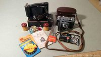 Overview photo showing both vintage Kodak cameras, their cases, user manuals, filters, Kodaguide booklet, Telesar lens and film canisters.