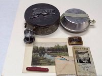 Photo showing the outdoor cook set with pewter basin, tin, small lantern, Swiss Army knife, belt buckle, guide book, and colorized river photo.