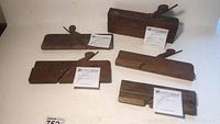 Five antique wooden block planes arranged on a white background showing size and shape variations.