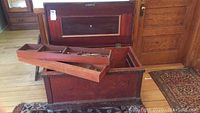Open antique wooden carpenter's chest showing three removable compartment trays inside, trunk lid open.