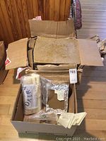 Two cardboard boxes containing beeswax slabs, formed cylinders, plastic molds, wicks