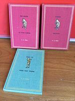 Three small vintage hardcover books with cloth covers: two red (The House at Pooh Corner and Winnie the Pooh) and one blue (When We Were Very Young) with gold embossed titles and illustrations.