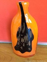 Front side of the vintage ceramic vase showing bright orange glaze and black drip decoration.