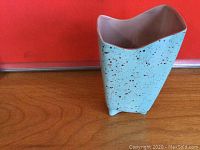 Side angled view of turquoise speckled ceramic vase with four feet on wooden surface.