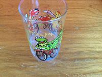 Front view of clear glass tumbler with colorful Kermit the Frog on bicycle illustration