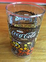 Front view of a vintage Coca-Cola clear glass decorated with colorful floral patterns and the Coca-Cola logo.