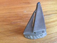 Side angle image of small brass sailboat figurine on wooden surface.