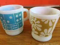 Pair of vintage Fire King mugs, one with blue domino tiles and one with yellow daisies.