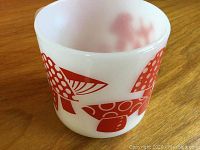 Side view of white glass coffee mug with red toadstool mushroom illustrations showing the detailed print of multiple mushroom shapes.