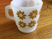 Side view of a small white milk glass mug decorated with yellow daisy flowers, showing the handle and overall pattern.