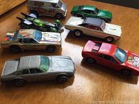 Group of seven vintage Hot Wheels diecast cars with various colors and wear displayed on wood surface.