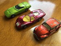 Three vintage die-cast cars shown from above on wooden surface: green gull-wing sports car, red race car, orange Volkswagen Beetle.