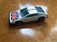 White Hot Wheels Lotus Royal Flash diecast car with Union Jack and Lotus logo decals on hood viewed from top and side angles on wood surface.