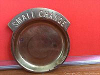 Top view of round brass coinage dish against red background showing 'SMALL CHANGE' embossed on raised rim.
