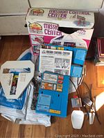 Overview of Mission Control Center components and original box placed on wooden floor.