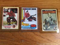 Three vintage Tony Esposito hockey cards from Chicago Black Hawks, placed side by side on wood surface, cards in sleeves.
