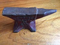 Side view of small heavy cast iron anvil with embossed 'HERCULES ANVIL CO NY' text on side, resting on wooden surface.