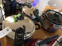 View showing two stainless steel pressure cookers (Presto and Revere) and a Crock-Pot brand slow cooker on wooden table.