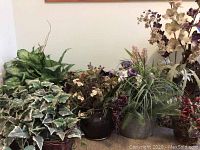 Wide view of assorted faux plants and flowers in various containers showing faux ivy, flowering plants, and foliage