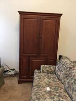 Front view of media center cabinet showing closed paneled doors and floral couch beside it