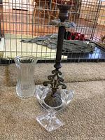 Photo showing a dark metal candlestick holder with ornate base, clear glass vase with textured diamond pattern, and a clear glass single candle holder with square base.