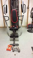 Front view of Weider Pro 4300 weight bench with cable arms and padded seat and backrest. Orange and metal dumbbells on floor in front.