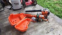 General view of Stihl blower, chainsaw and open orange plastic case on concrete floor