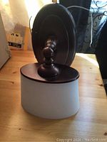 Photo of the wall light fixture showing the bronze or dark metal backplate and frosted glass shade on a wooden surface.