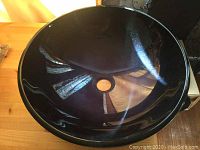 Top view of round blue glass vessel sink showing central drain hole and blue glossy reflective surface.